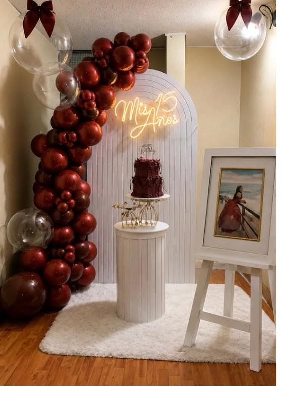 Decoración de quince años en tonos vino y dorado con arco de globos